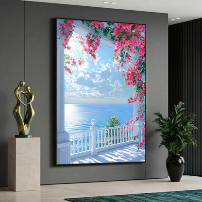 A view of a blue ocean and bright sky with white clouds from a white balconied terrace with columns, framed by vibrant pink bougainvillea flowers hanging from above.