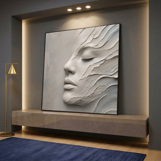 A square canvas wall art showing a minimalist 3D-effect female face in cream and beige colors, styled on a marble console in a modern room.